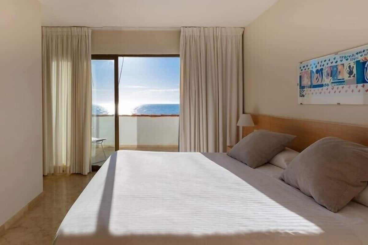A hotel room with a large bed, a view of the sea, and a painting on the wall.