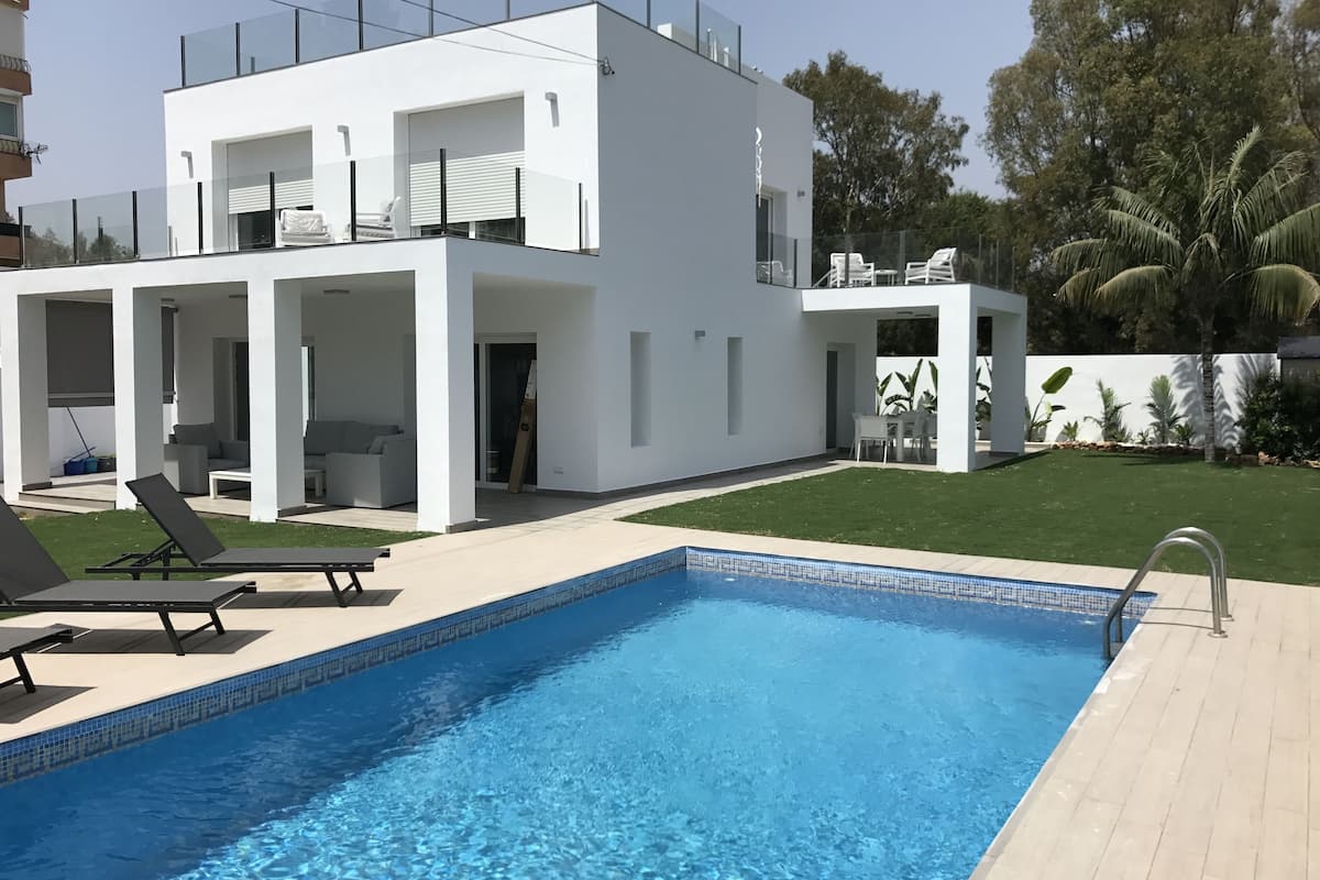 A modern two-story house with a swimming pool, outdoor seating, and a well-maintained lawn.