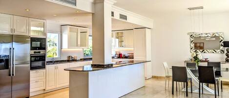 A modern kitchen with a central island, stainless steel appliances, and a dining area with a chandelier.