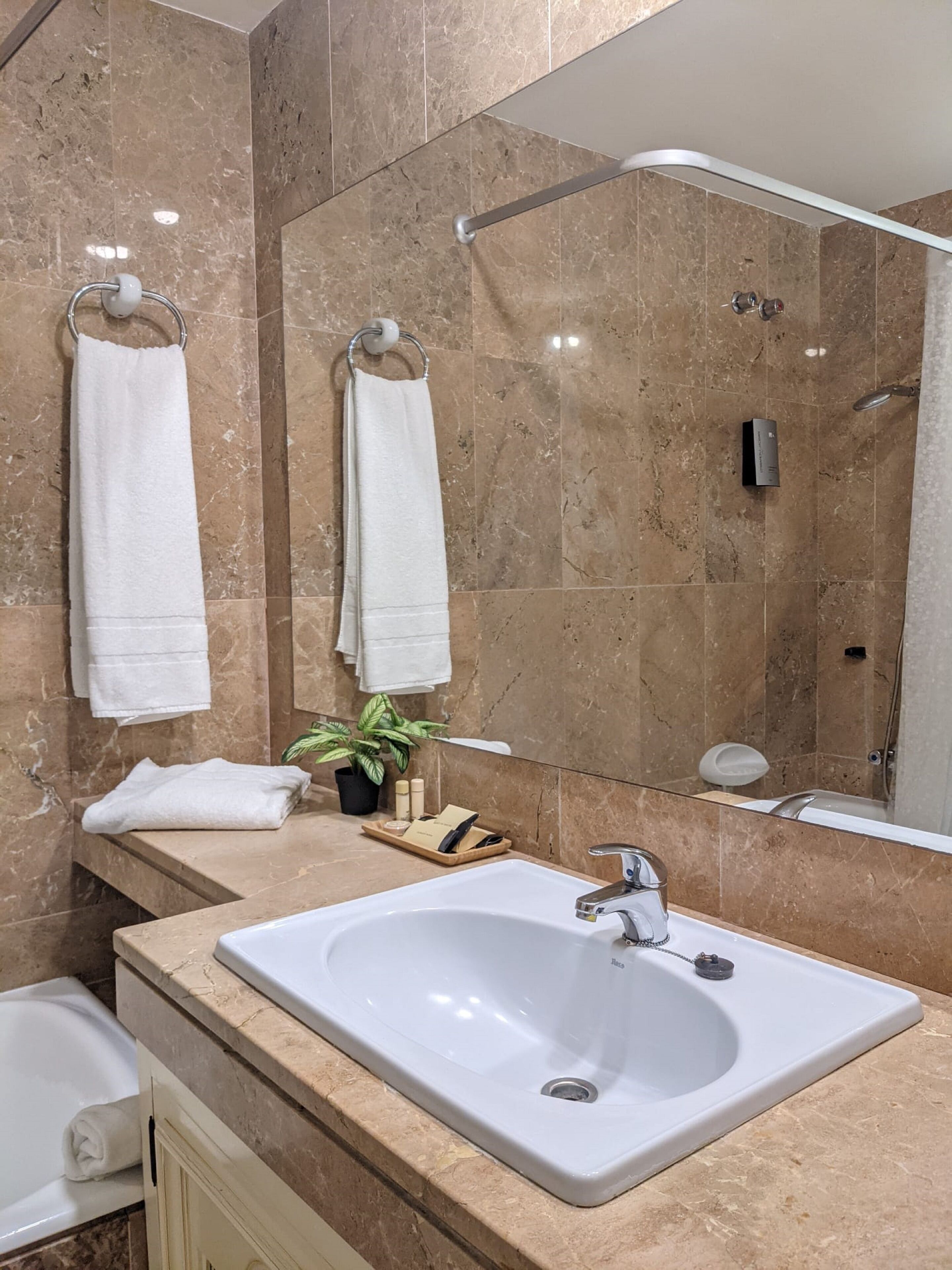 A bathroom with a large mirror, a sink, and two towels hanging on towel racks.