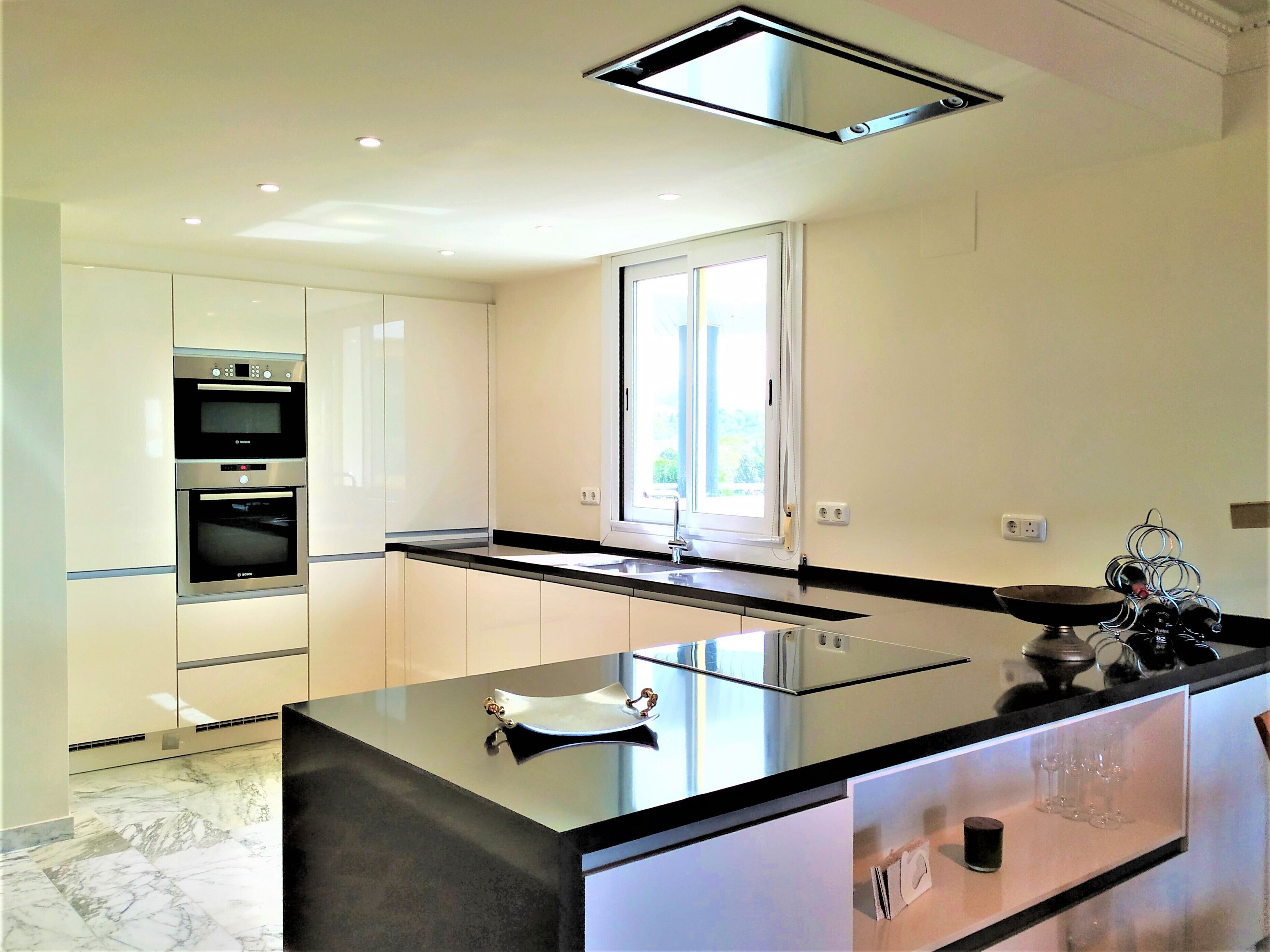 A modern kitchen with a central island, built-in ovens, and a window providing natural light.