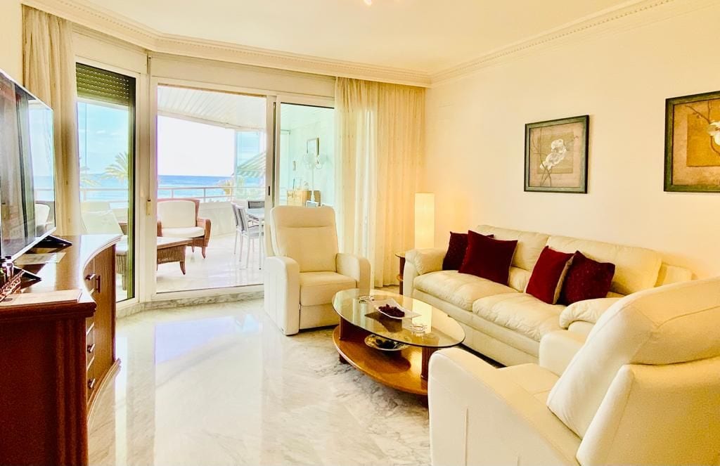A hotel room with a sofa, armchairs, a glass coffee table, and a television.