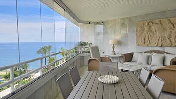 A balcony with a view of the ocean, a dining table, and seating arrangements.