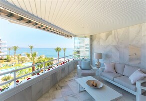 Een balkon met uitzicht op zee, een bank, een tafel en een lamp.