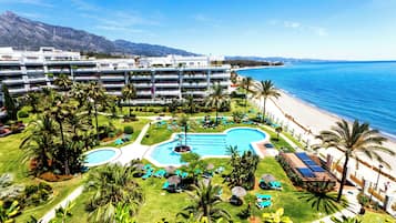 Relax by the pool surrounded by lush greenery and palm trees, with stunning views of the adjacent beach and sea.