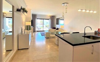 Een moderne keuken met een centraal eiland, een zithoek met een bank en stoelen, en een uitzicht op de omgeving door grote ramen.