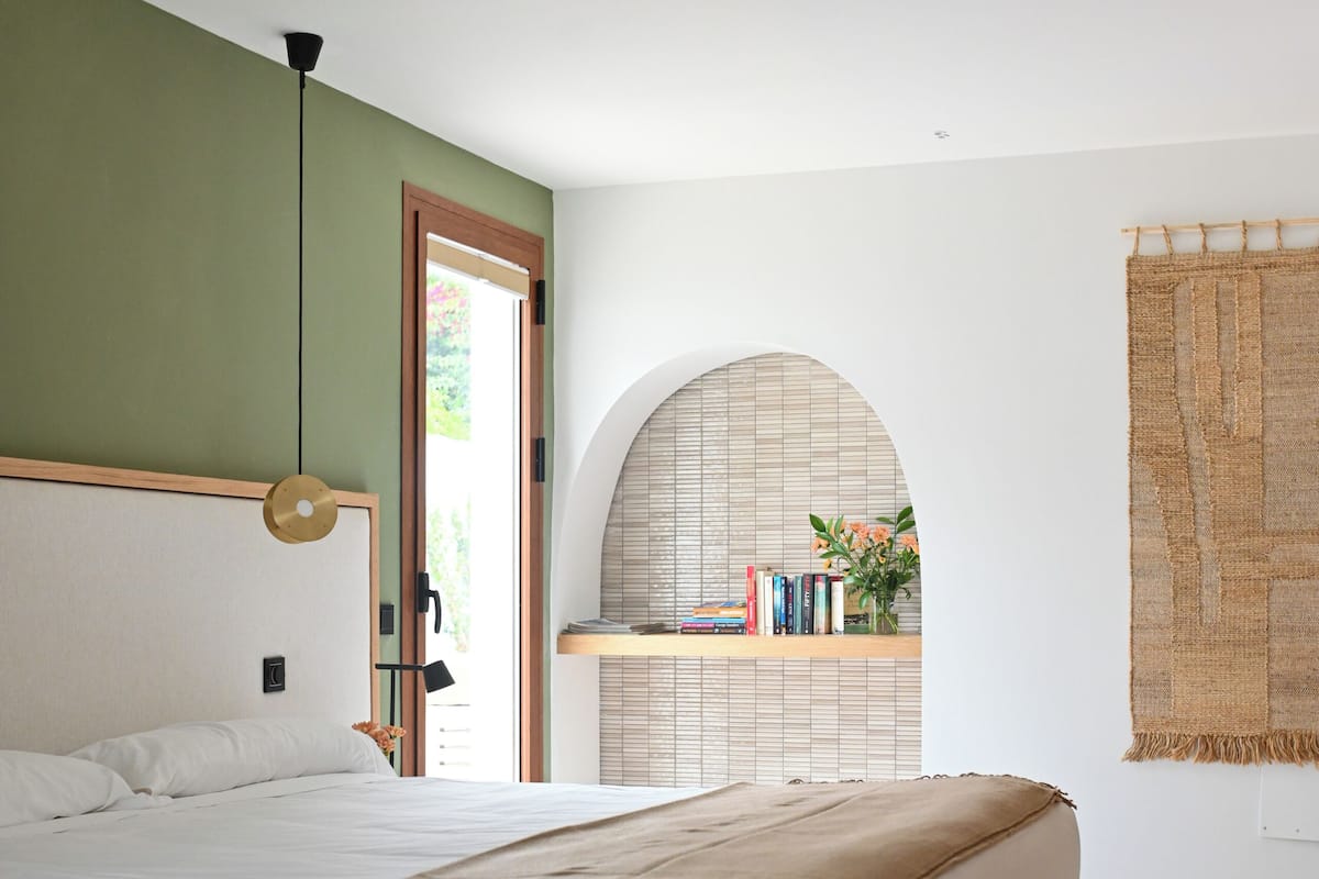 A bedroom with a bed, a hanging light, a bookshelf, and a window.