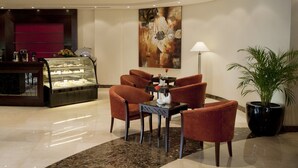 A lobby with a marble floor, a glass display case with desserts, a table with chairs, a painting on the wall, and a potted plant. - Musherib Hotel (Doha)