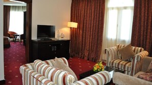 A hotel room with a TV, a sofa set, a coffee table, and a large window with curtains. - Musherib Hotel (Doha)
