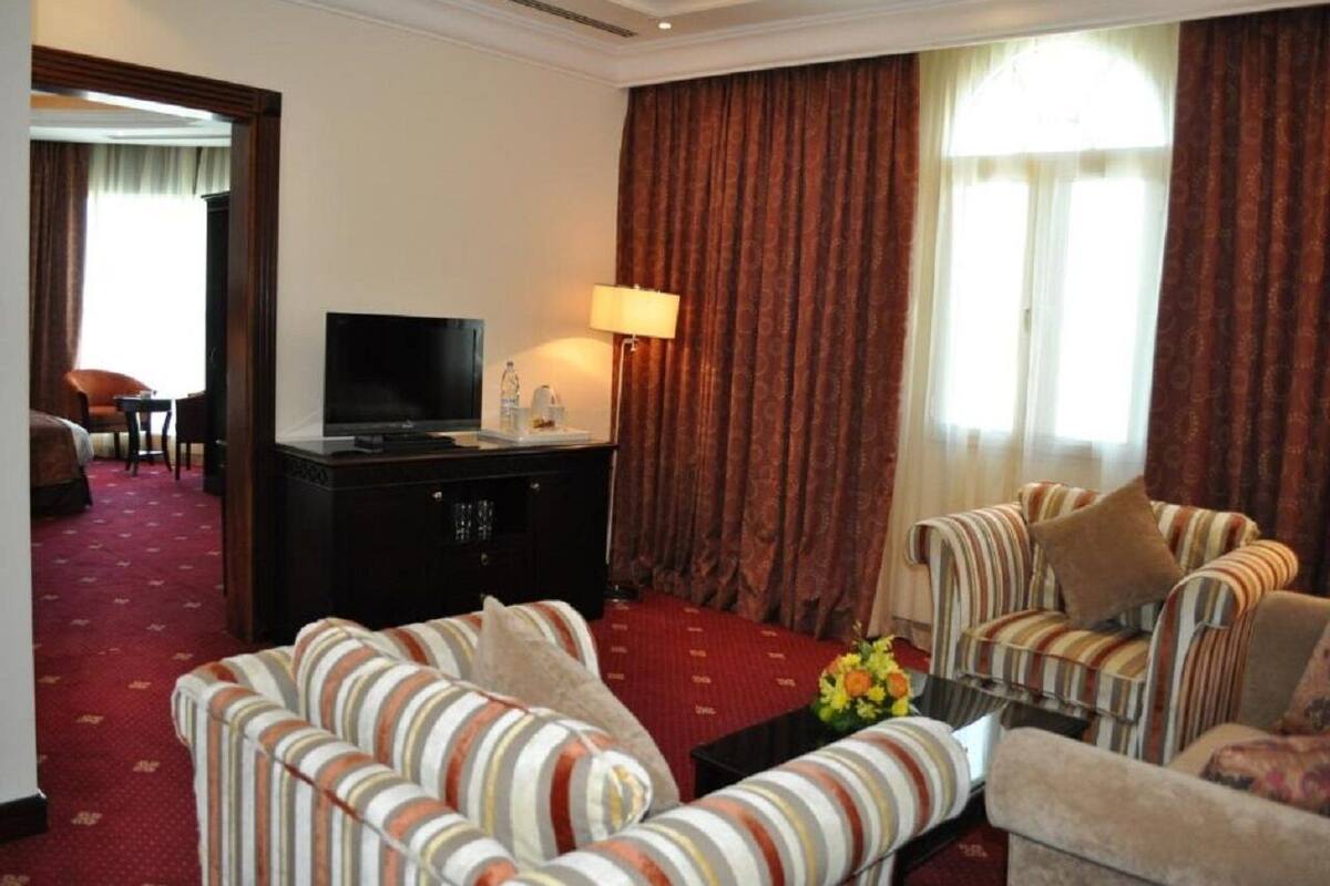 Une chambre d’hôtel équipée d’une télévision, d’un canapé, d’une table basse et d’une grande fenêtre avec des rideaux.