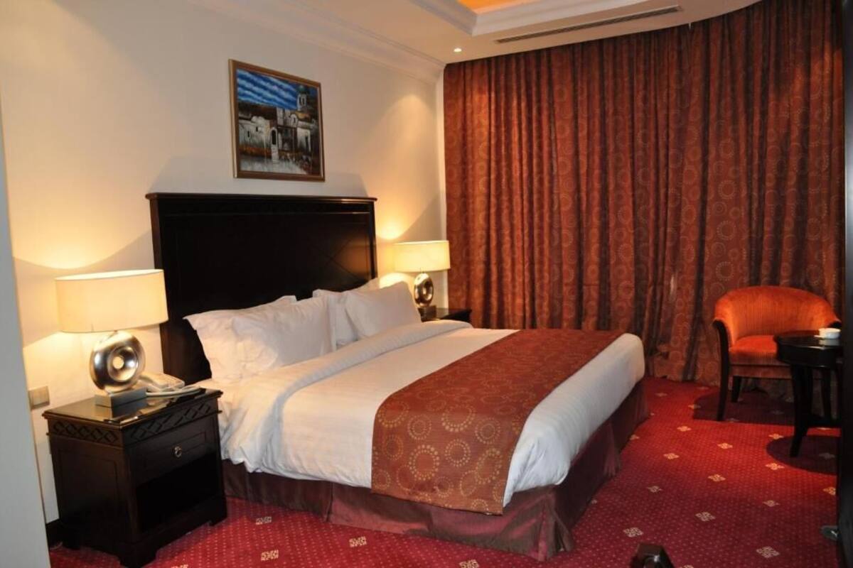 Une chambre d’hôtel avec un grand lit, deux tables de chevet avec des lampes, une chaise et un tableau au mur.