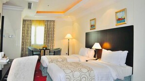 A hotel room with two beds, a desk, a chair, a lamp, and a painting on the wall. - Musherib Hotel (Doha)