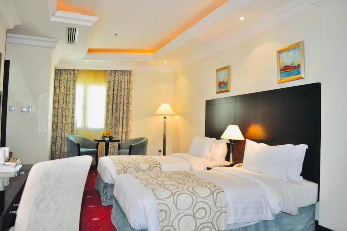 Une chambre d’hôtel avec deux lits, un bureau, une chaise, une lampe et un tableau au mur.