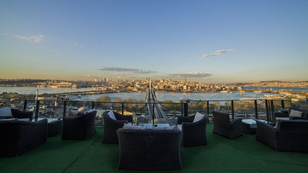 A terrace with wicker furniture and a view of a cityscape across a river. - HHK Hotel (Istanbul)
