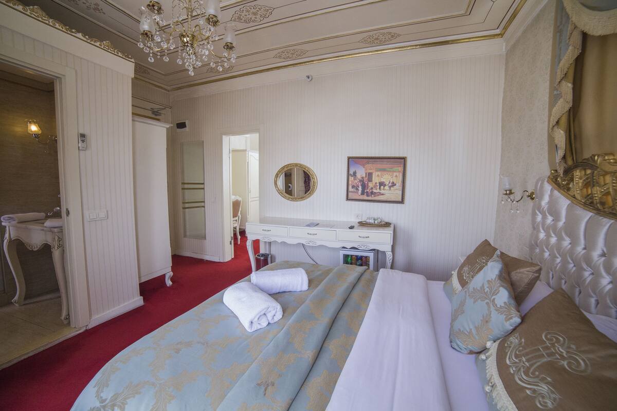 A hotel room with a bed, a vanity with a mirror, a desk, and a chandelier.