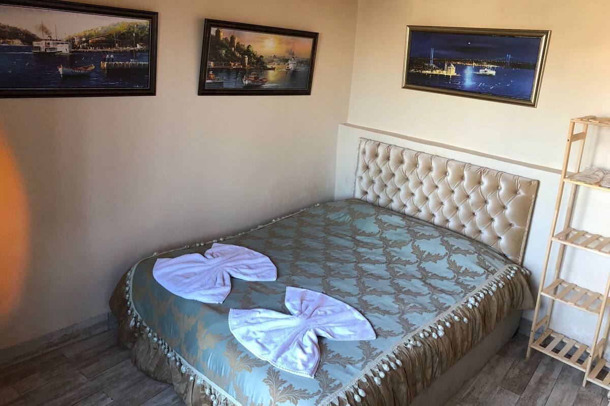 A bedroom with a bed, a headboard, a wooden shelf, and three framed pictures on the wall.