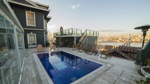 A rooftop swimming pool with a city view, a glass-enclosed room, and a deck with outdoor furniture. - HHK Hotel (Istanbul)