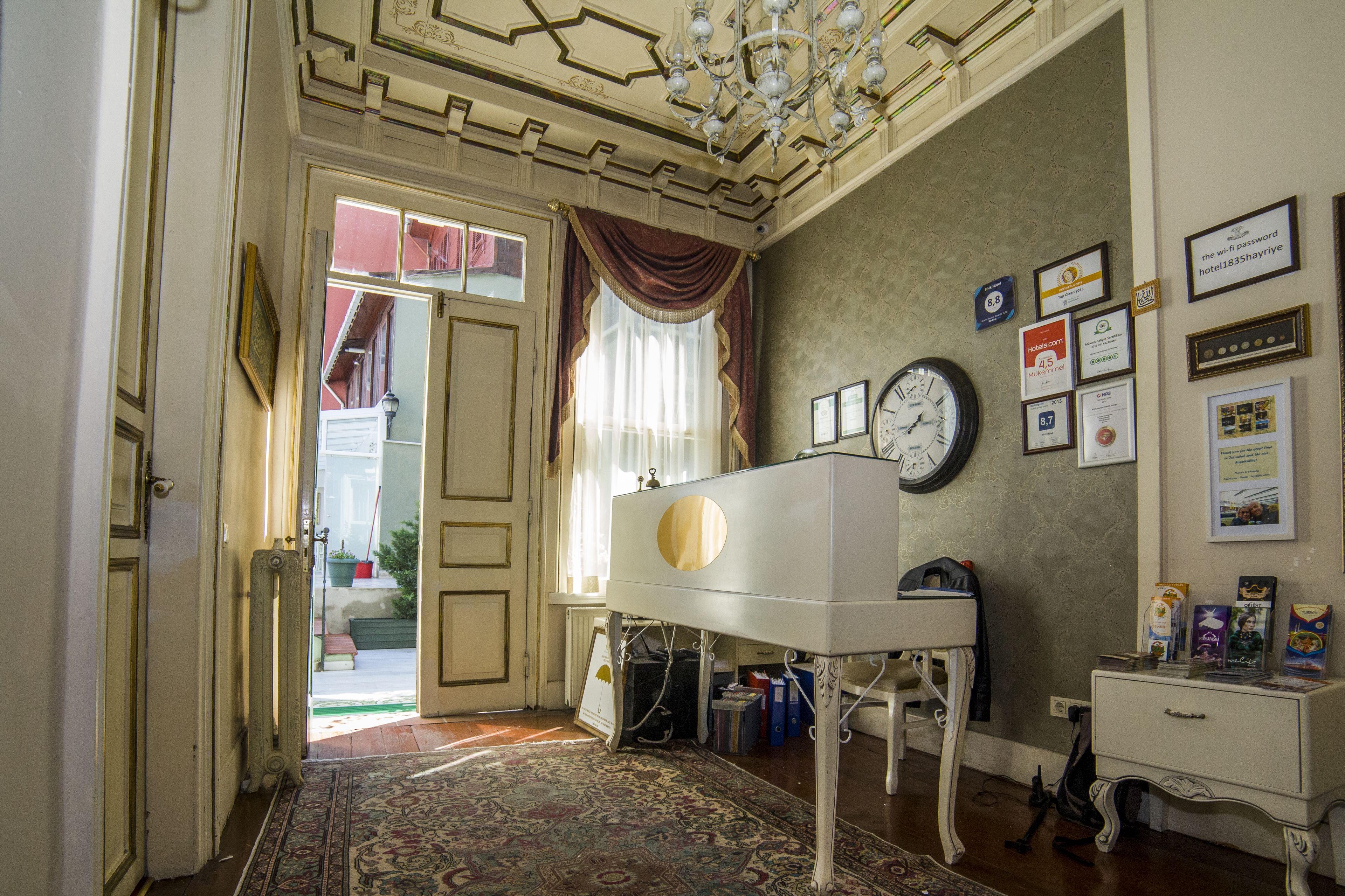 Une pièce avec un piano, une horloge et divers certificats encadrés accrochés au mur.