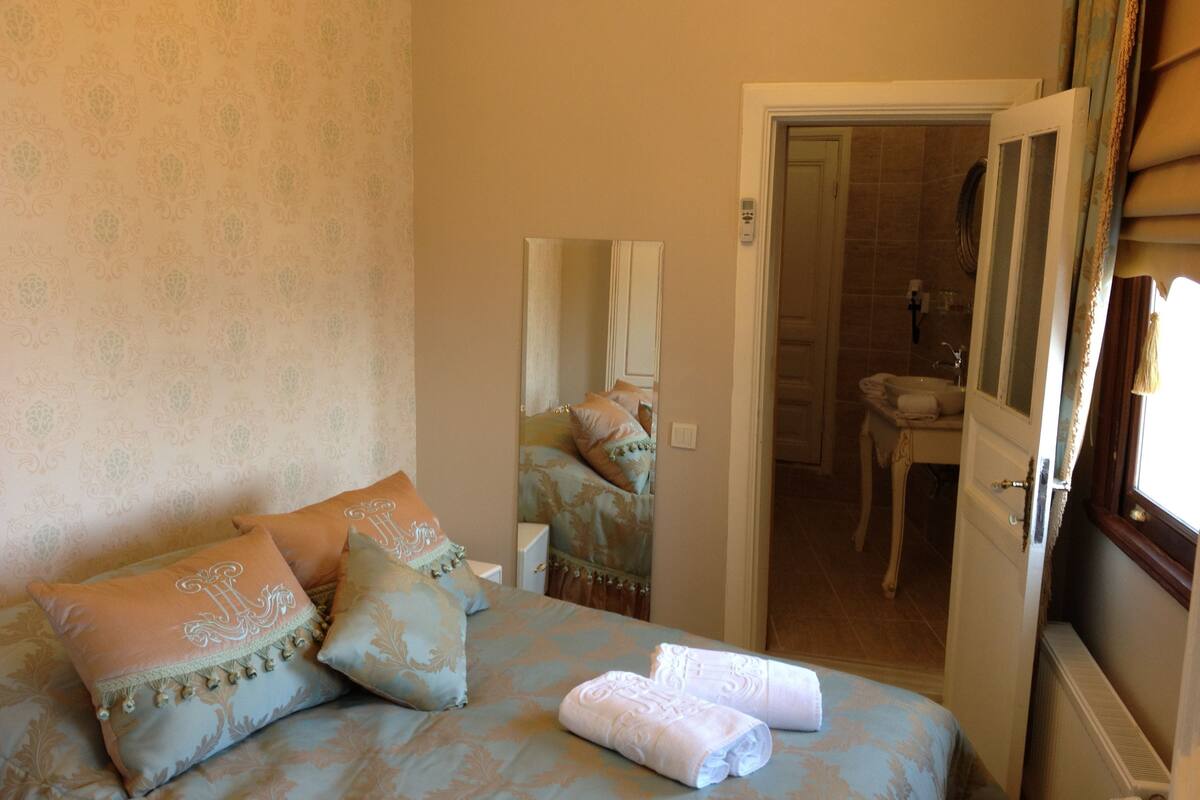 A bedroom with a bed, pillows, a mirror, and a bathroom visible through an open door.