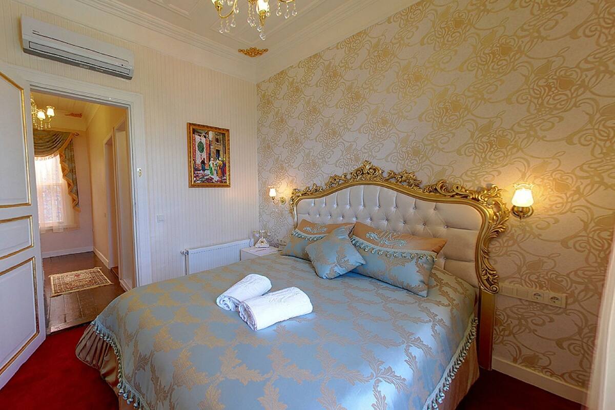 A bedroom with a large bed, a chandelier, and a painting on the wall.