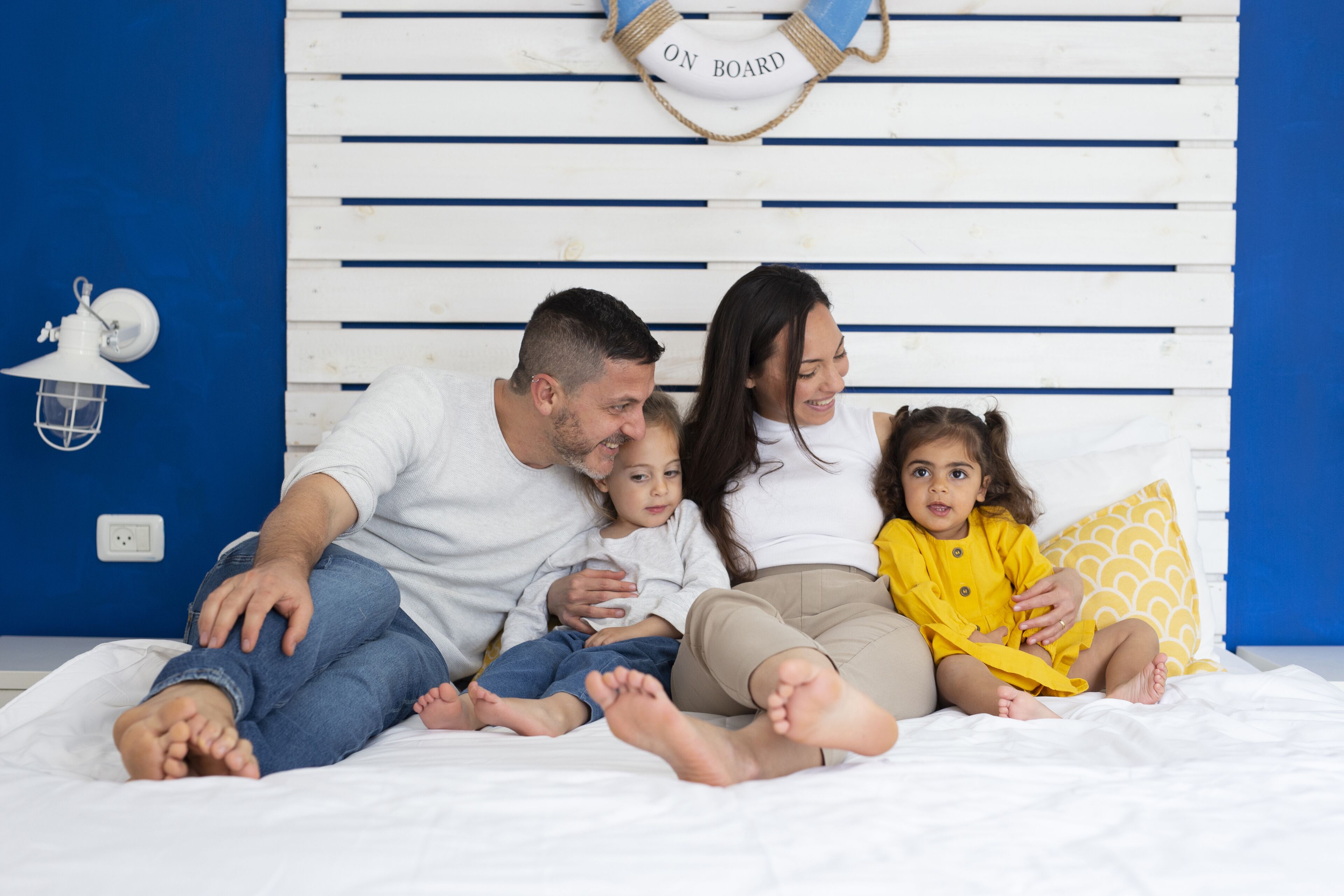 A family sitting on a bed with a white headboard and a blue wall.