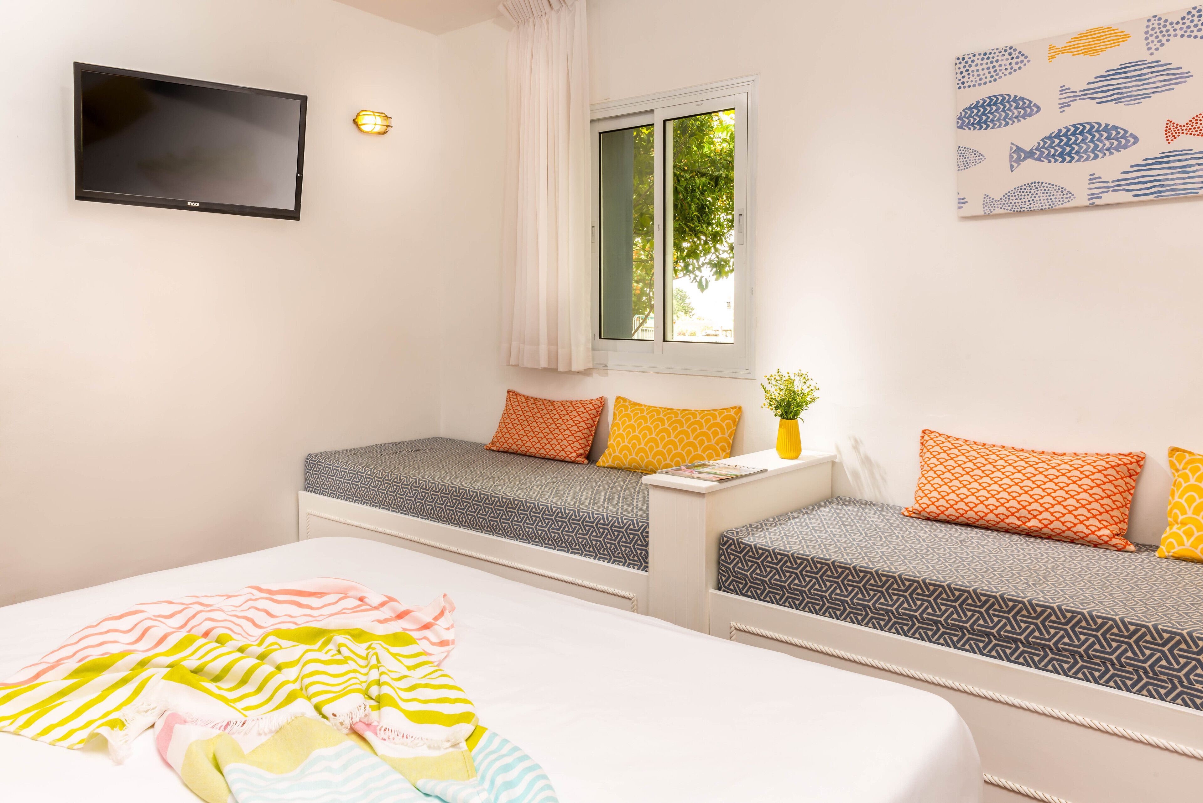 A bedroom with two beds, a TV, a window with curtains, and a wall art piece.