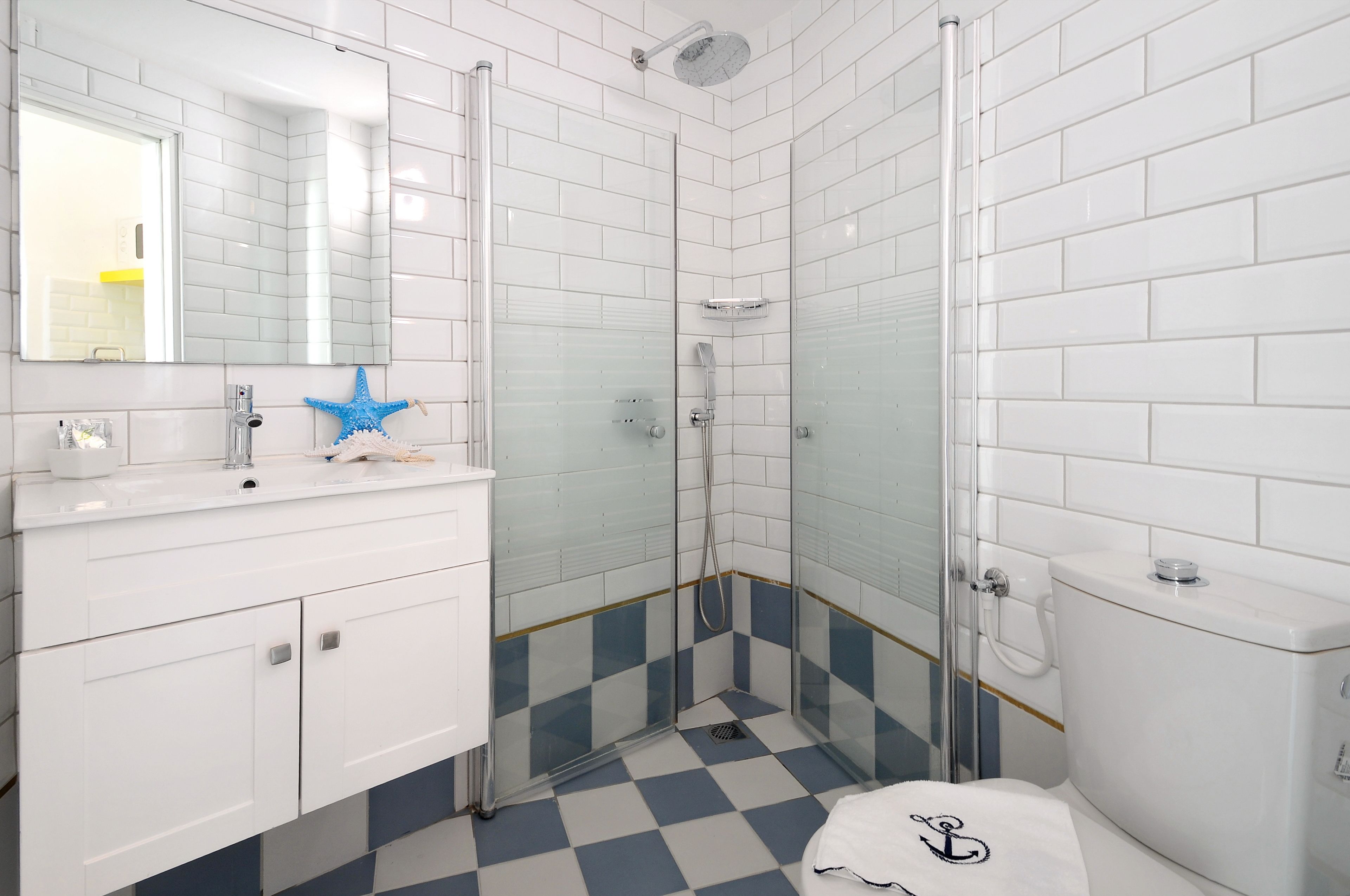 A bathroom with white tiled walls, a blue and white checkered floor, a glass shower enclosure, a white sink with a blue star decoration, and a white toilet.