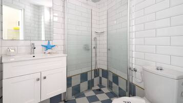 A bathroom with white tiled walls, a blue and white checkered floor, a glass shower enclosure, a white sink with a blue star decoration, and a white toilet.