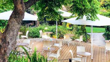 An outdoor patio with tables and chairs, surrounded by greenery and trees.