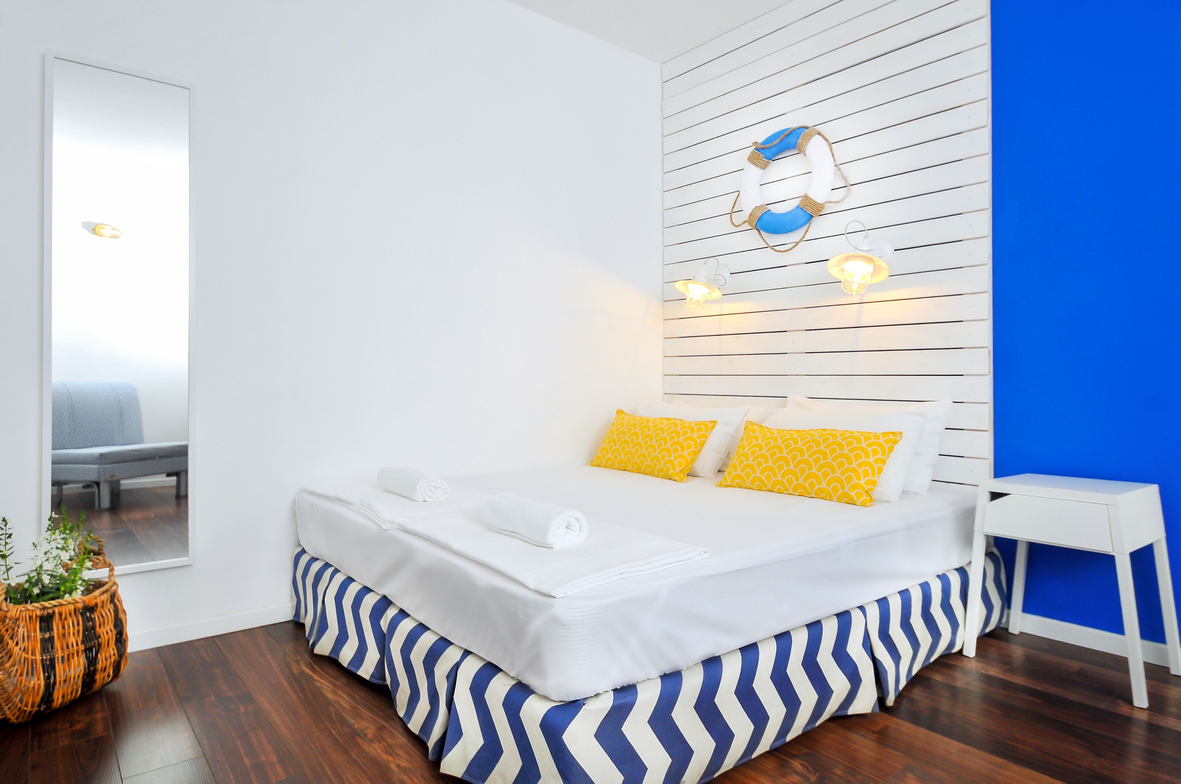 A neatly made bed with white linens and blue and white striped bedding, a small bedside table, and a wall-mounted light fixture with a blue and white design.