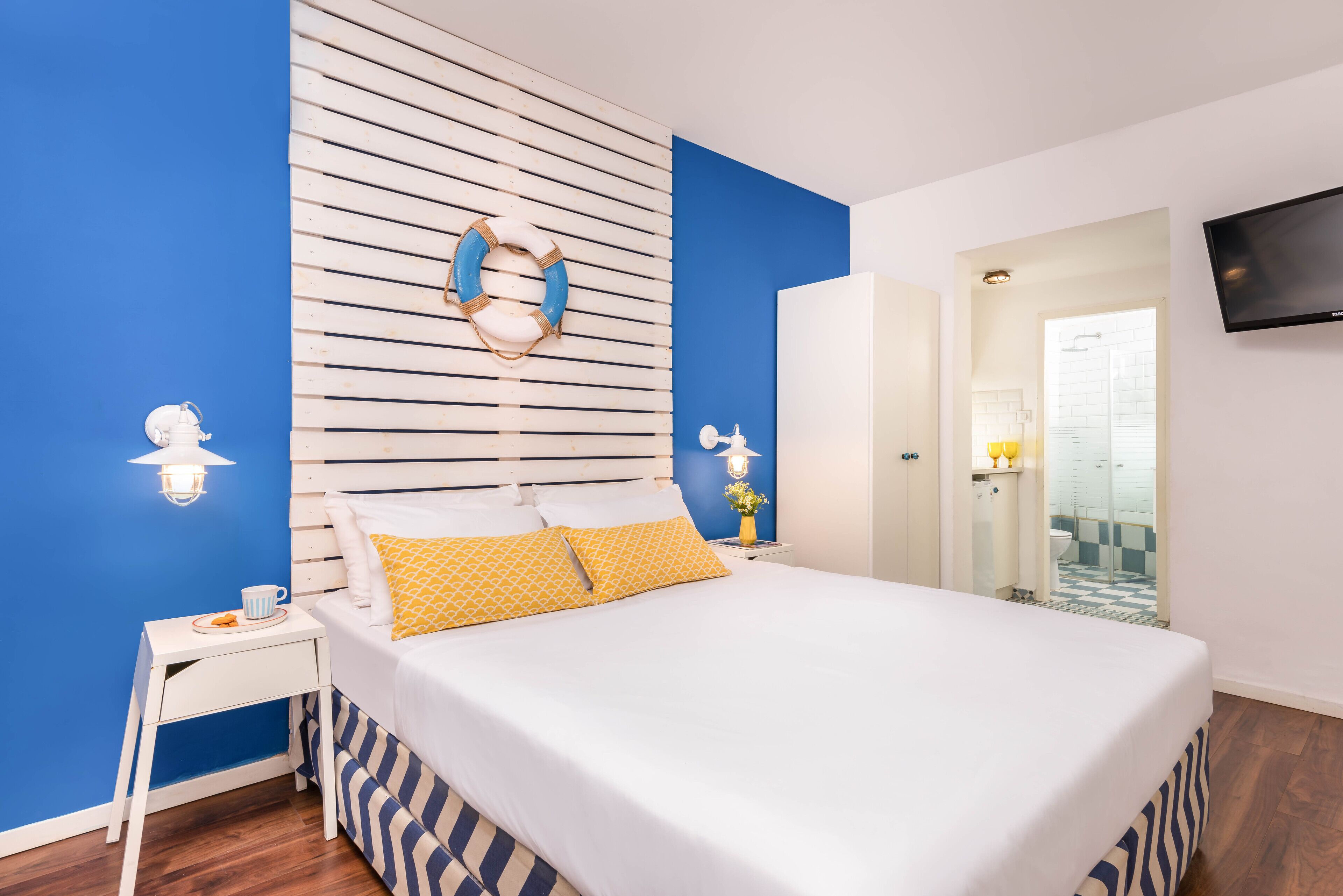 A bedroom with a bed, a nightstand, a wall-mounted TV, and a bathroom visible through an open door.