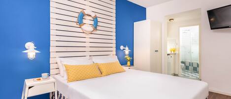 A bedroom with a bed, a nightstand, a wall-mounted TV, and a bathroom visible through an open door.