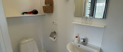 A small, clean bathroom with a toilet, sink, and a mirror above the sink. There is a towel rack and a small shelf with a basket.