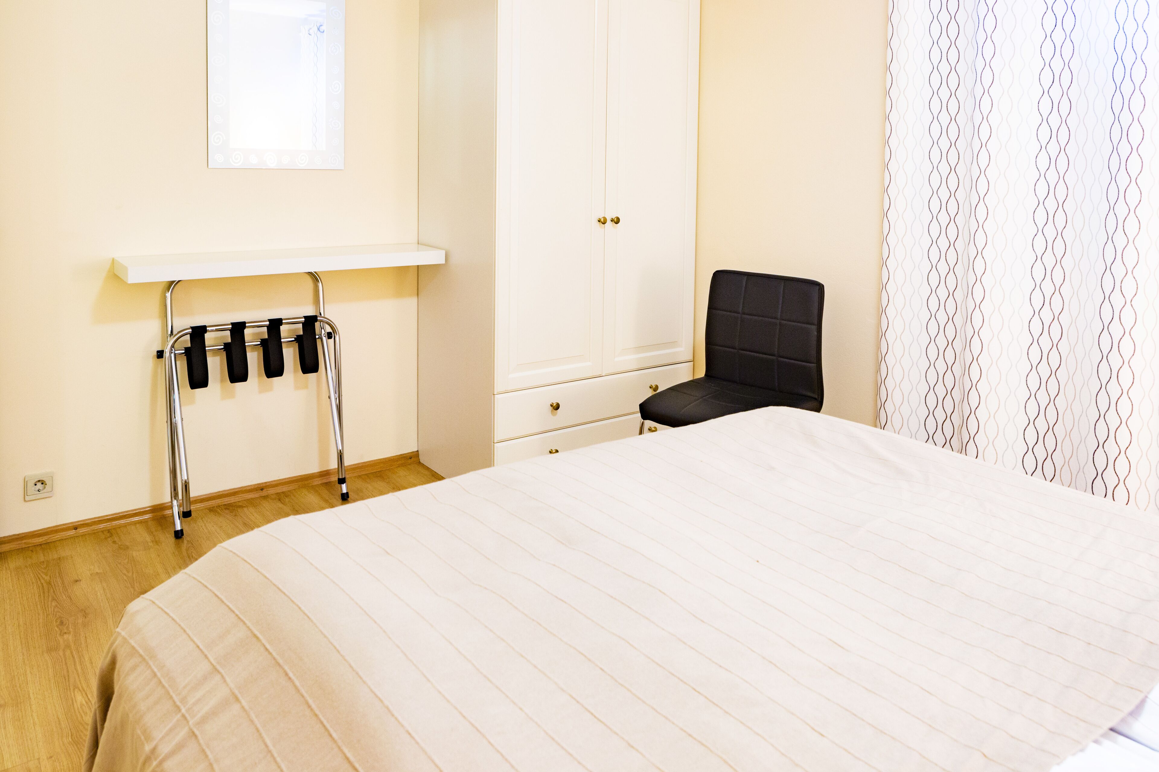 A bedroom with a bed, a wardrobe, a chair, and a shelf with a towel rack.