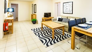 A modern living room with a sofa, a wooden coffee table, a TV, and a dining table set for two. - Guesthouse Sunna (Reykjavik)