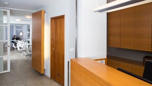 A hotel reception area with a wooden reception desk, a closed door, and a view into a dining area with white tables and chairs. - Guesthouse Sunna (Reykjavik)