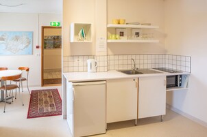 Una cocina moderna con armarios blancos, lavavajillas, un fregadero y microondas. Hay una zona de comedor con una mesa y sillas, y una alfombra en el suelo.