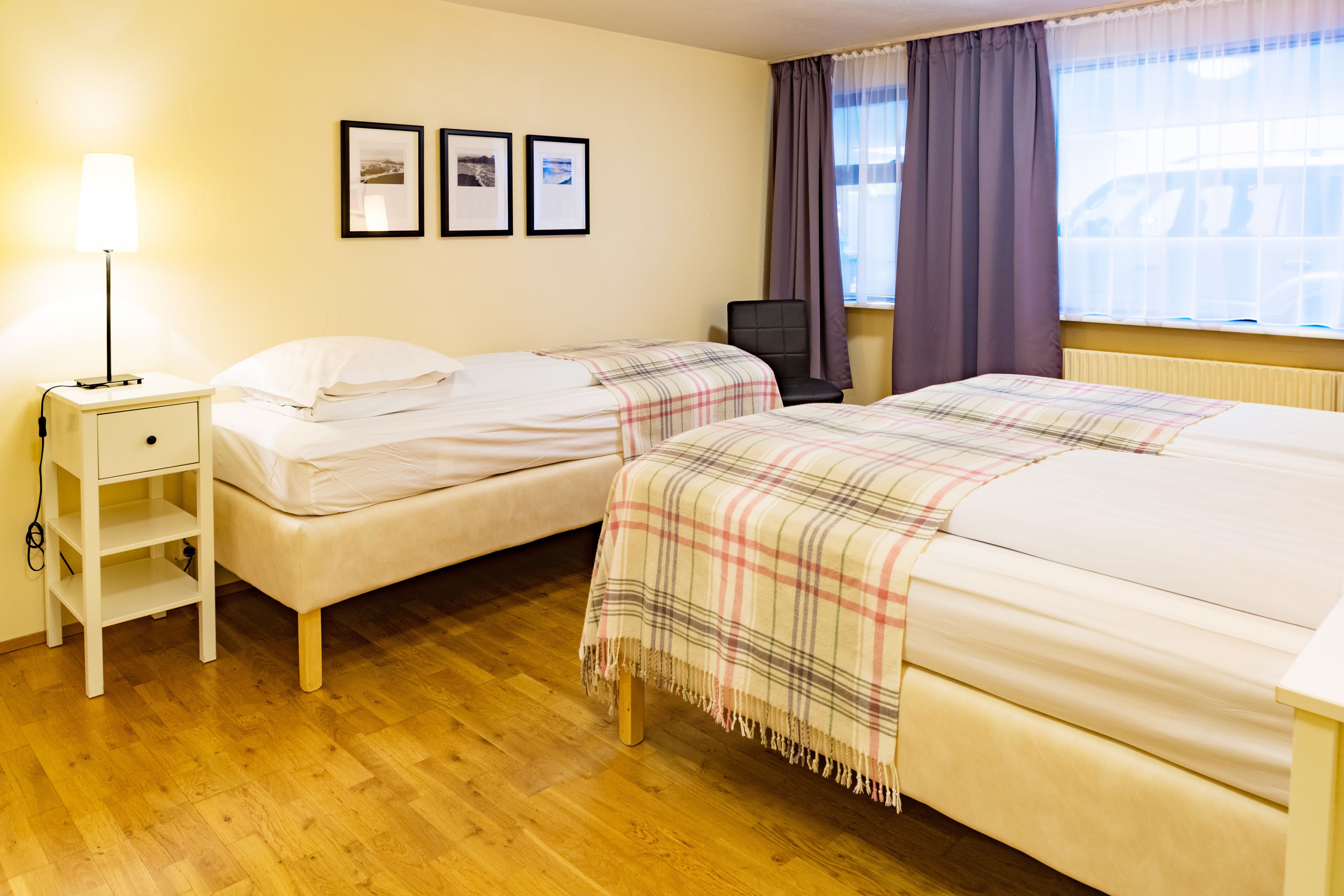 Ein Hotelzimmer mit zwei Betten, einem Nachttisch, einem Stuhl und einem Fenster mit Vorhängen.