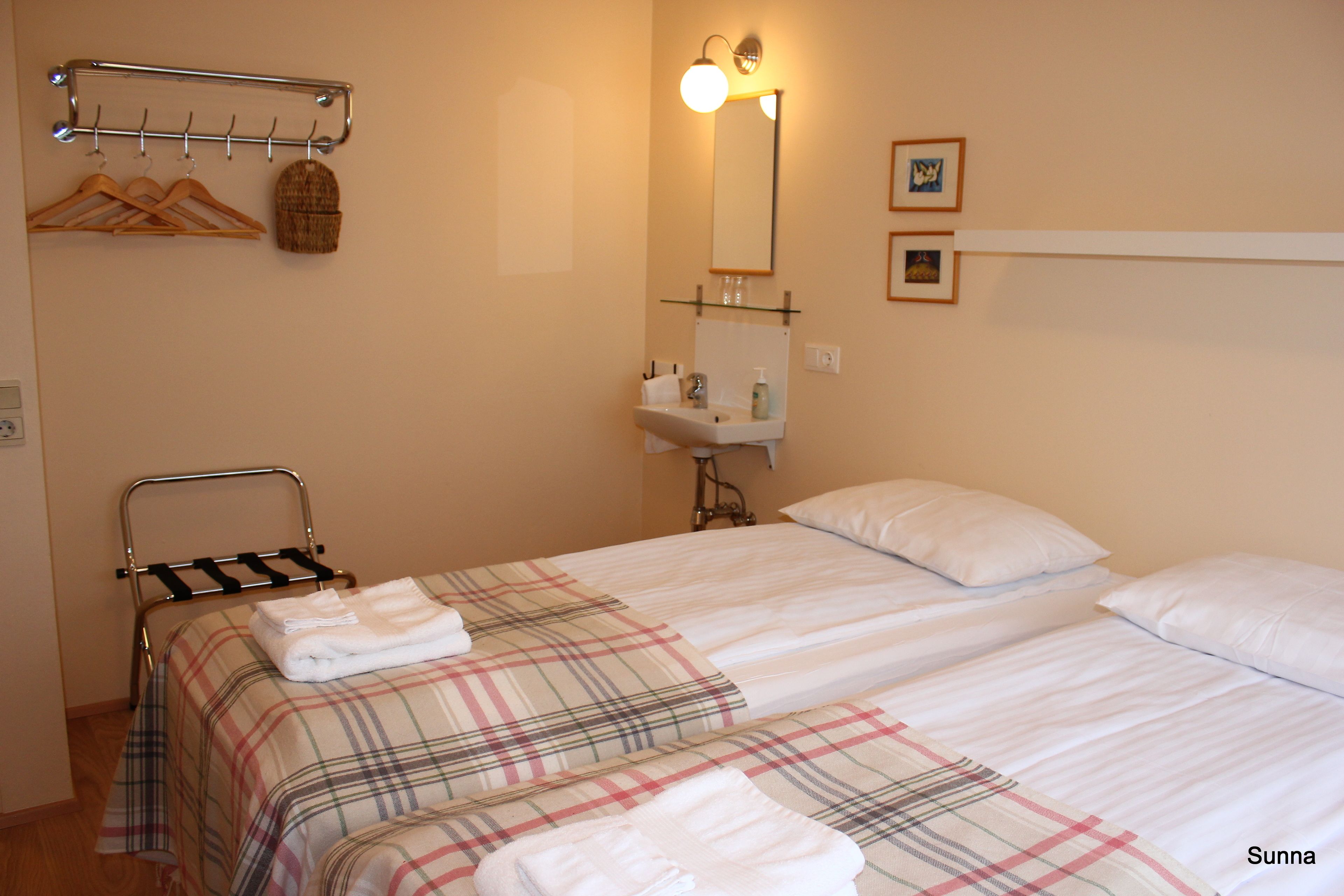 A hotel room with two beds, a bathroom with a sink and mirror, and a coat rack with hangers.