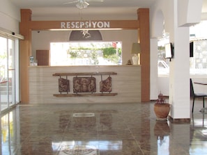 Un área de recepción con piso de mármol pulido, un mostrador de recepción y un letrero que dice "RESEPSIYON".