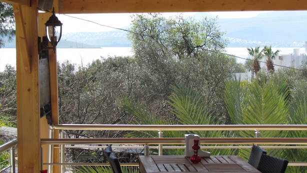 A wooden balcony with a table and chairs, overlooking a body of water and greenery. - Ministar Hotel (Bodrum)