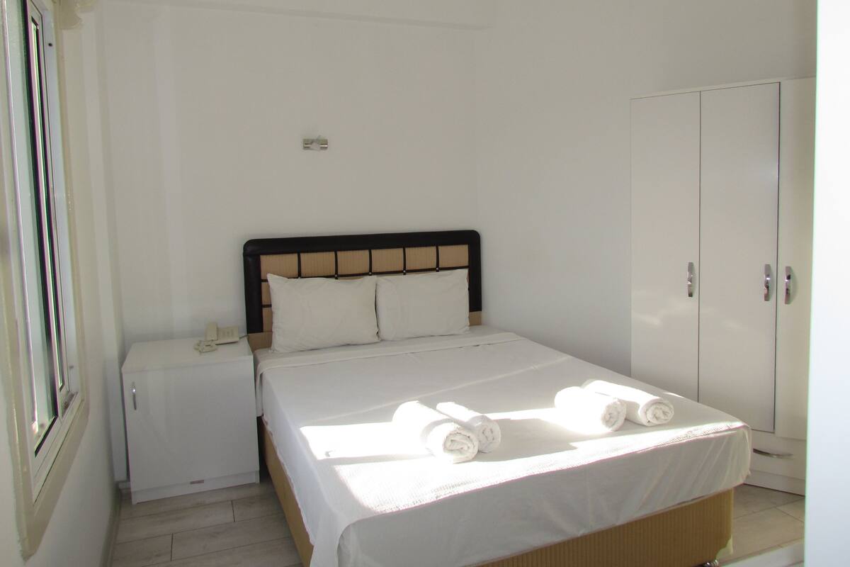 A bedroom with a bed, a nightstand, a wardrobe, and a window.