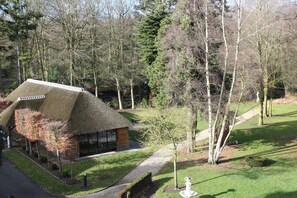 A thatched-roof building with a glass facade, surrounded by a well-maintained garden and tall trees. - Hotel Lodewijk Van Male (Bruges)