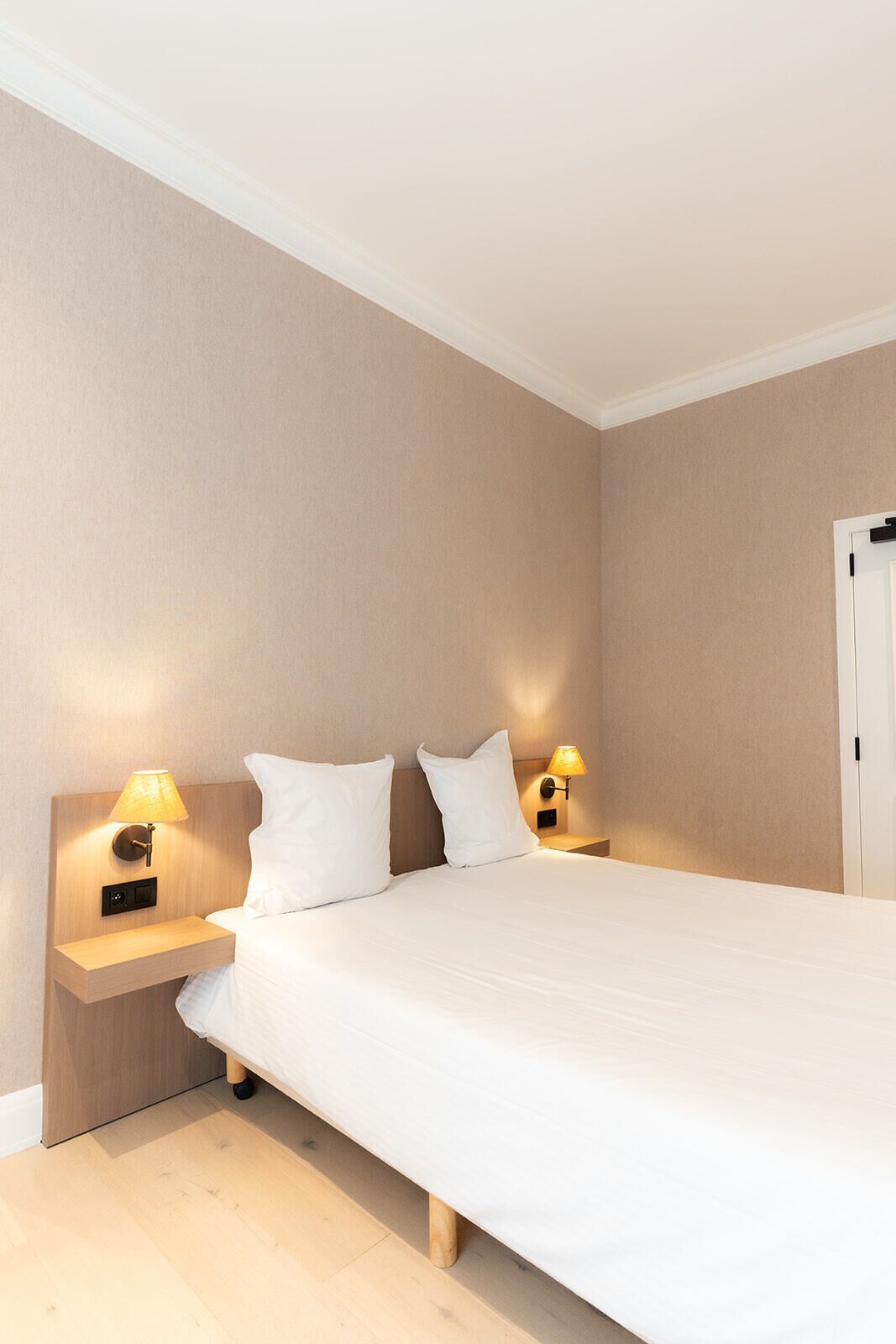 Et hotelværelse med en stor seng, to sengeborde med lamper og en dør til højre.