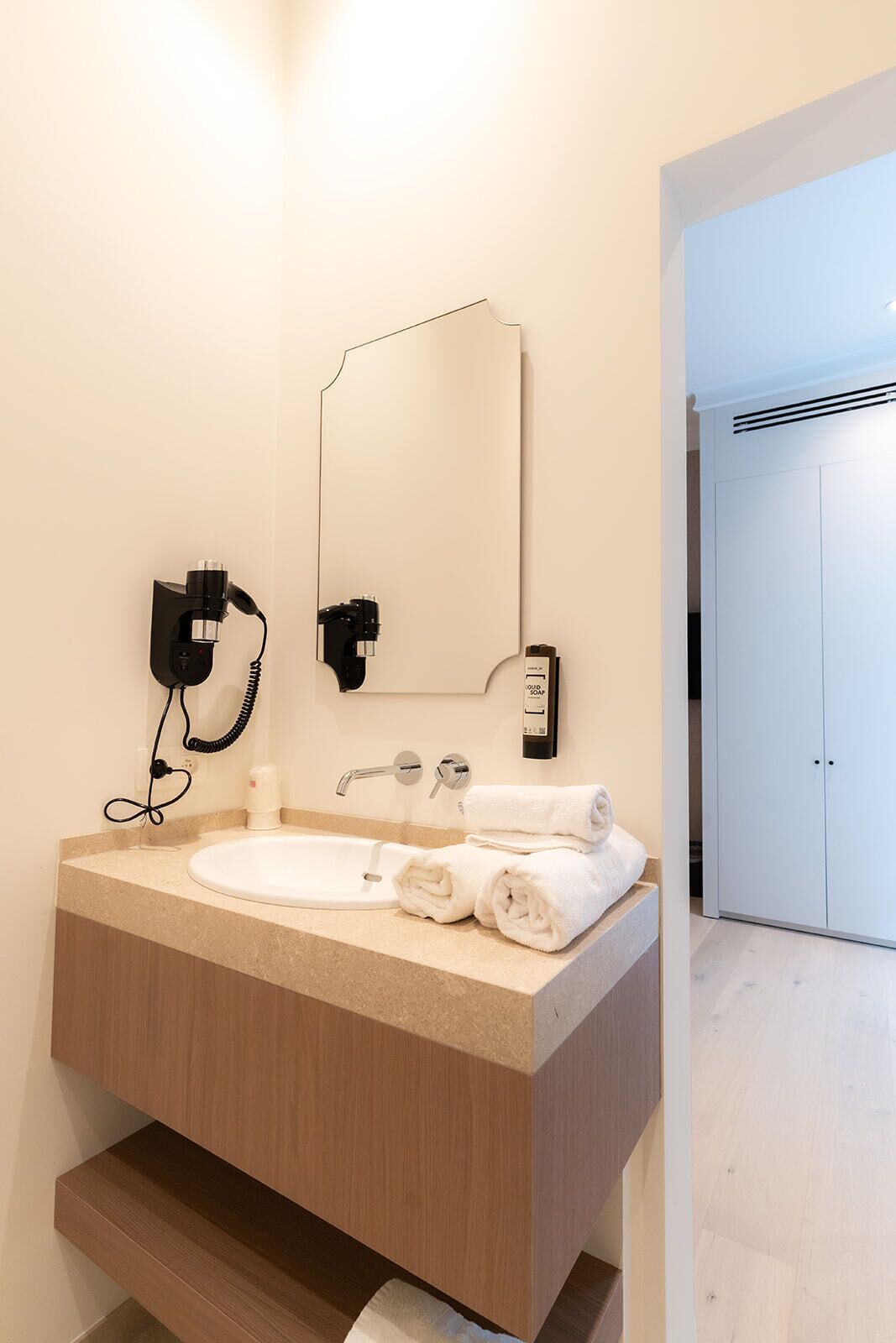 Un baño moderno con lavamanos, espejo, toallero y secador de pelo.