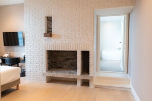 A hotel room with a white brick fireplace, a flat-screen TV mounted on the wall, a bed, and a view of the hallway. - Hotel Lodewijk Van Male (Bruges)