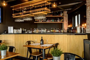 Een bar met houten kasten vol flessen en glazen, een houten toonbank en tafels met stoelen.