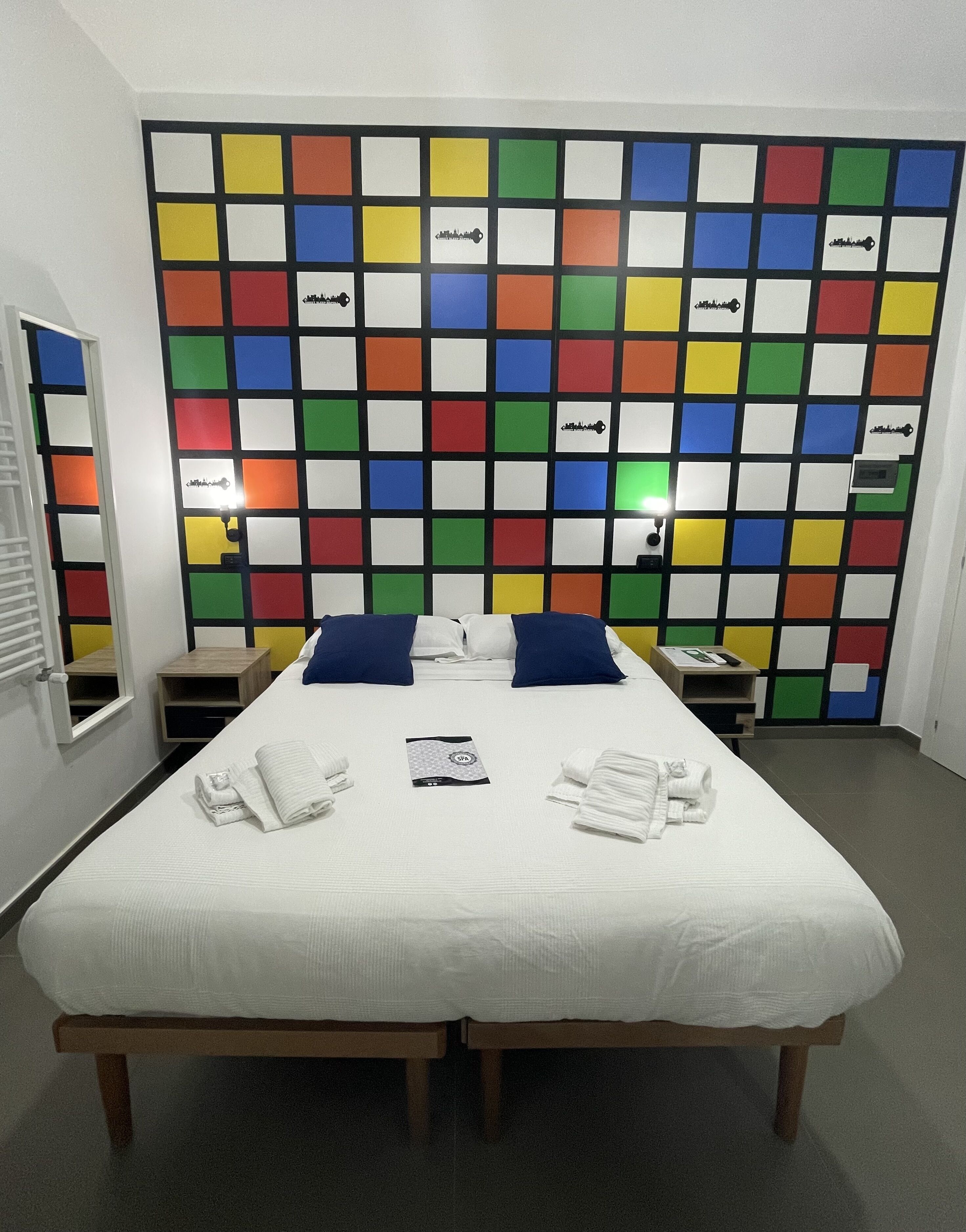 Habitación de hotel con una cama grande, dos almohadas, una mesita de noche y un panel de pared colorido.