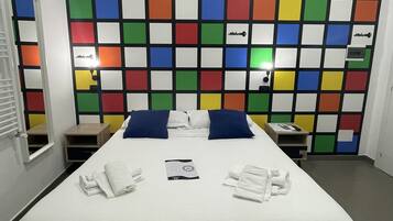 Habitación de hotel con una cama grande, dos almohadas, una mesita de noche y un panel de pared colorido.