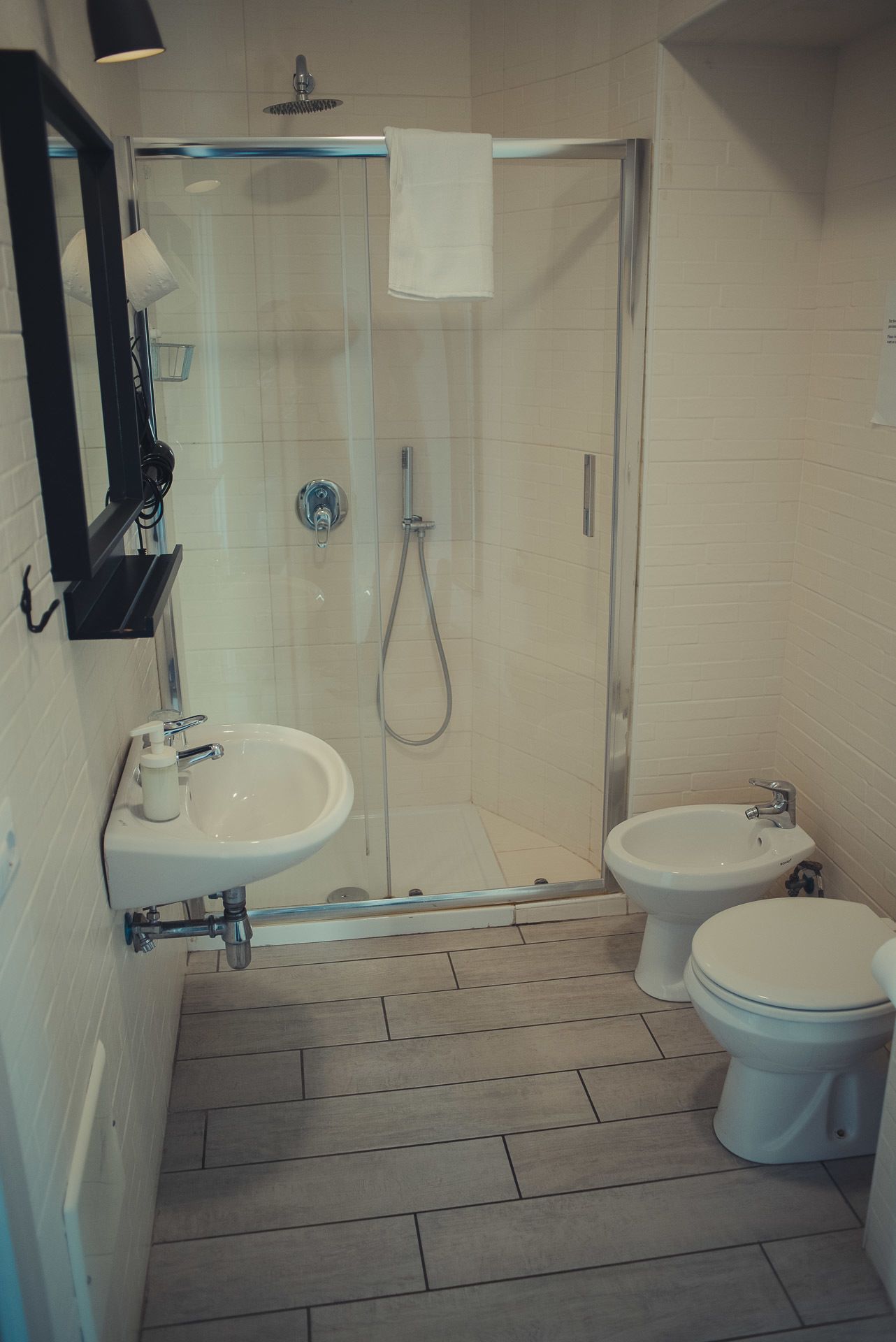 Un baño pequeño con ducha acristalada, lavamanos y dos inodoros.